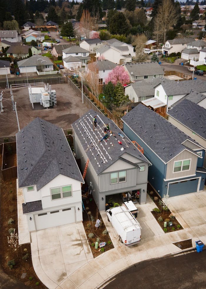 gallery-05 Drone shot of workers installing new roof panels in a suburban neighborhood.